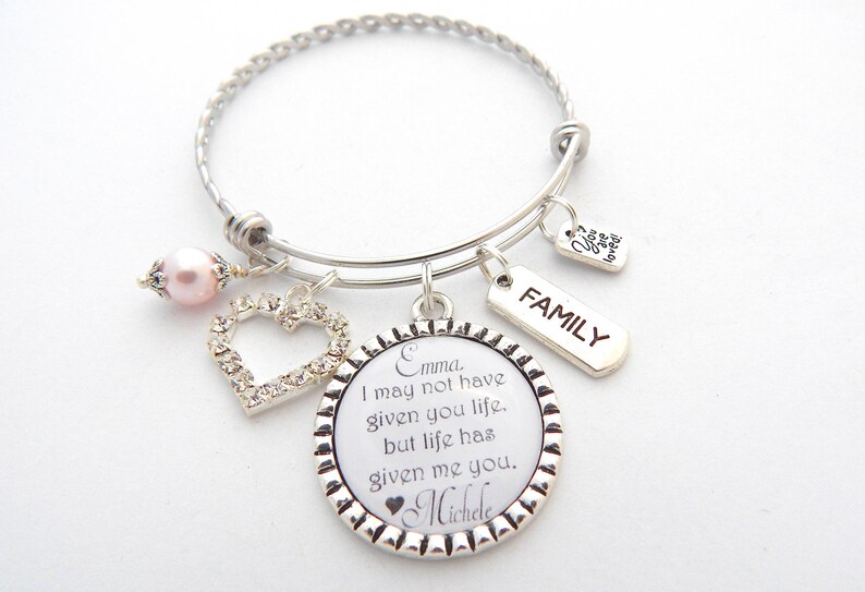 May include: Silver charm bracelet with a heart charm, a pearl, and a round charm with the text "Emma. I may not have given you life, but life has given me you. Michele". The bracelet also has a tag that says "FAMILY".