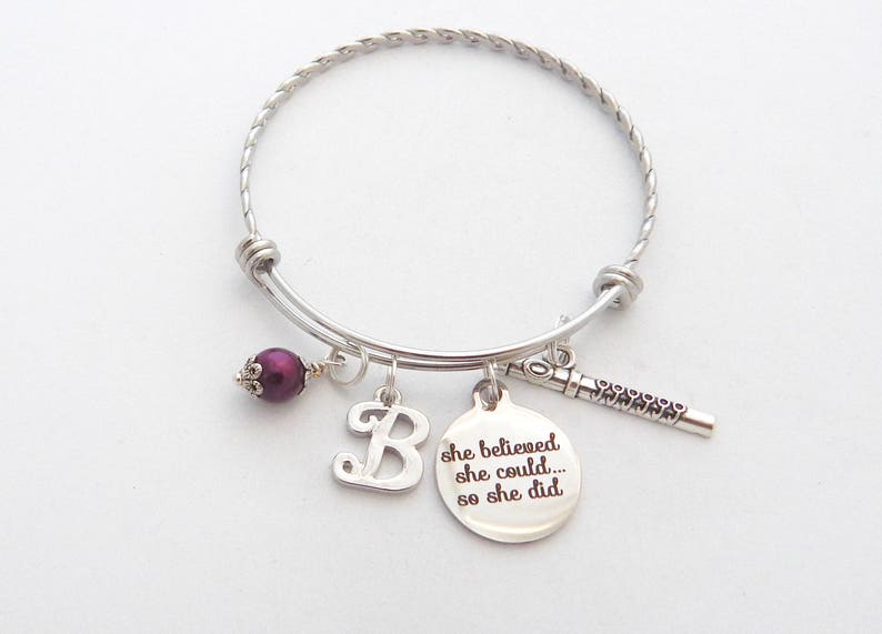 Peut inclure: Un bracelet jonc argent&eacute; avec une perle violette, un charme avec la lettre "B" et un charme avec le texte "She believed she could... so she did".