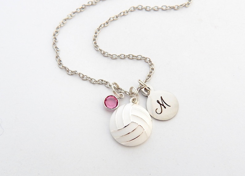 May include: Silver necklace with a volleyball charm, a pink crystal charm, and a silver charm with the letter "M" engraved on it.