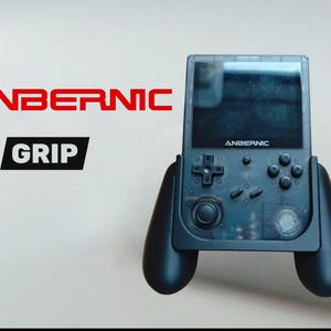 Può includere: Console di gioco portatile nera con la scritta "ANBERNIC" in rosso e "GRIP" in un riquadro nero. La console ha uno schermo trasparente e impugnature nere con pulsanti e un joystick.