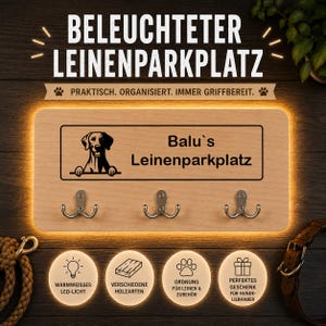 Könnte beinhalten: Ein rechteckiges Wandboard aus hellem Holz mit drei Metallhaken. Das Schild zeigt eine schwarze Hunde-Grafik und den Text "Balu's Leinenparkplatz". Das Board ist von einer warmweißen LED-Beleuchtung umrandet, die einen Lichtschein erzeugt.