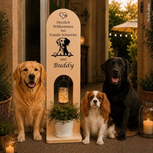 Könnte beinhalten: Ein hohes, oben abgerundetes Schild aus hellem Holz mit einer schwarzen Grafik eines Hundes, einem Herz mit Pfotenabdruck und dem Text "Herzlich Willkommen bei Familie Schneider und Buddy". Ein Glas mit Lichterkette hängt in einer Öffnung.