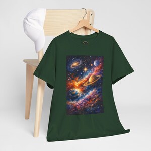 Puede incluir: Una camiseta de manga corta en color verde bosque oscuro con un estampado gráfico rectangular y vibrante del espacio exterior, que incluye una galaxia espiral, un planeta con anillos, un planeta azul y nebulosas coloridas sobre fondo negro.