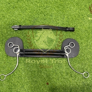 May include: A black leather horse bit with silver metal rings and curved bars. A matching black leather headstall is positioned above the bit. The items are displayed on a green surface.