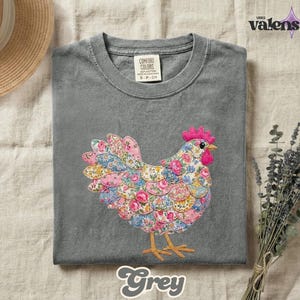 May include: A grey t-shirt featuring a colorful floral chicken design. The chicken is made of various floral patterns in pink, blue, and yellow. The shirt has a crew neck and short sleeves. The word "Grey" is written in a script font at the bottom.