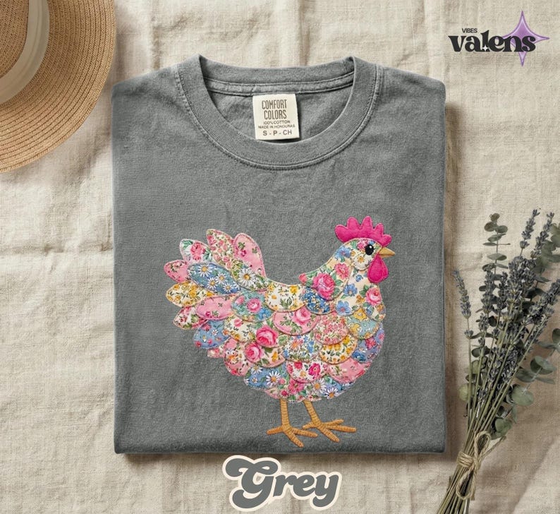 May include: A grey t-shirt featuring a colorful floral chicken design. The chicken is made of various floral patterns in pink, blue, and yellow. The shirt has a crew neck and short sleeves. The word "Grey" is written in a script font at the bottom.