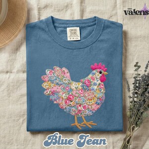 May include: Blue jean colored t-shirt with a floral chicken design. The chicken is made of pink, blue, and yellow floral fabric. The text "Blue Jean" is at the bottom of the shirt.