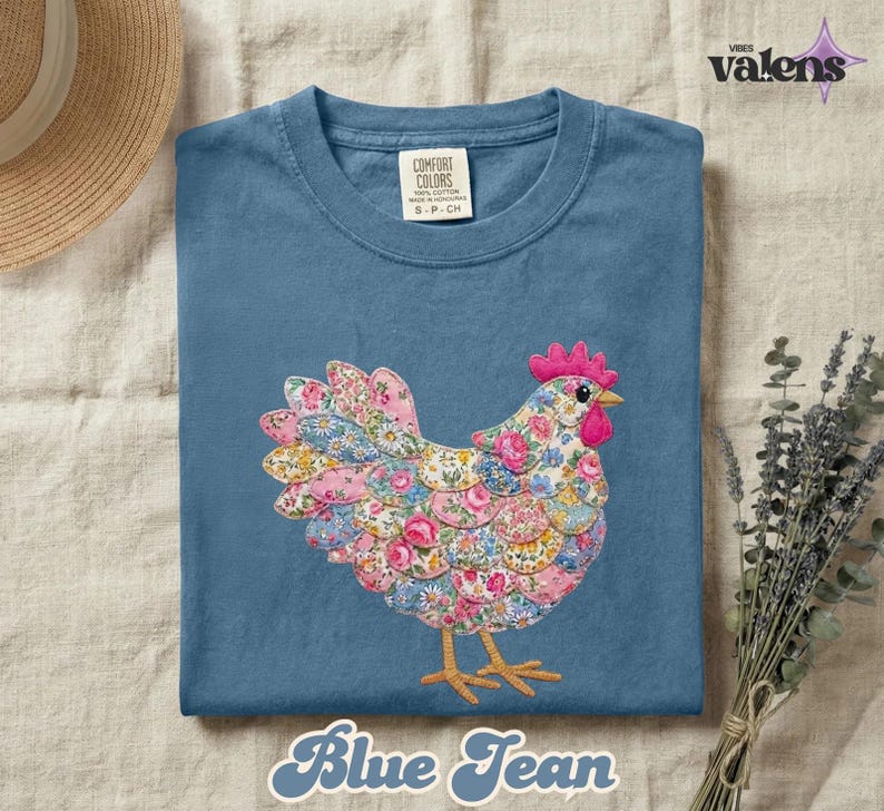 May include: Blue jean colored t-shirt with a floral chicken design. The chicken is made of pink, blue, and yellow floral fabric. The text "Blue Jean" is at the bottom of the shirt.