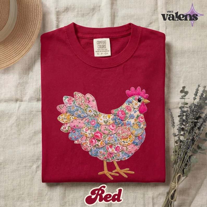 May include: A red t-shirt featuring a colorful floral chicken applique. The chicken has a pink comb and beak, with a body made of various floral patterns. The word "Red" is written in a cursive font at the bottom of the shirt.