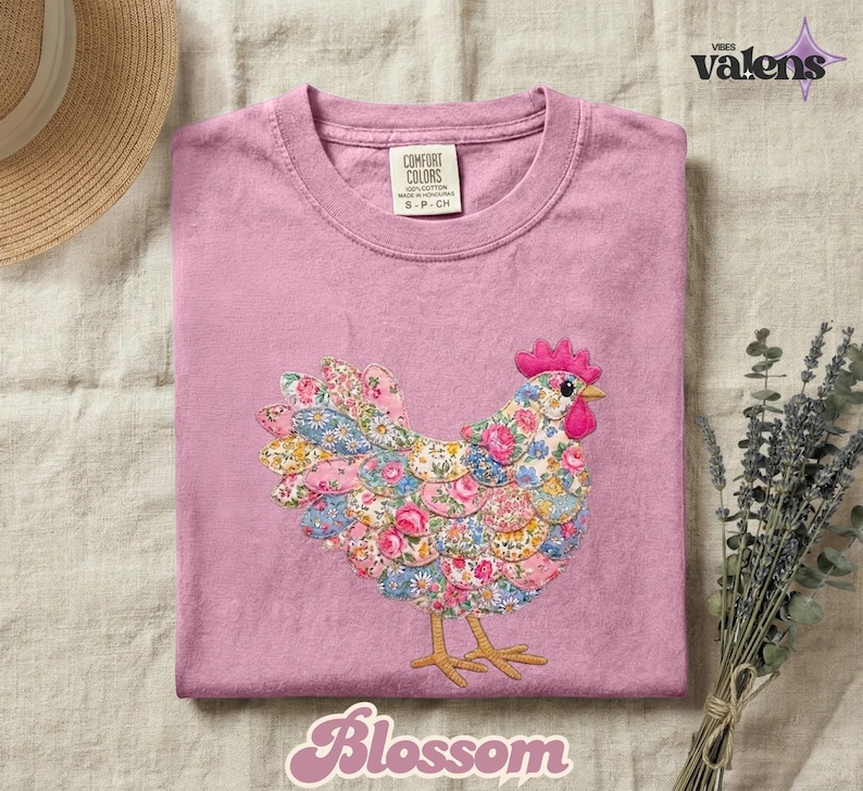 May include: A pink Comfort Colors t-shirt featuring an embroidered hen with a floral pattern in shades of pink, blue, and yellow. The hen has a red comb and beak. The word "Blossom" is written in a cursive font at the bottom of the shirt.