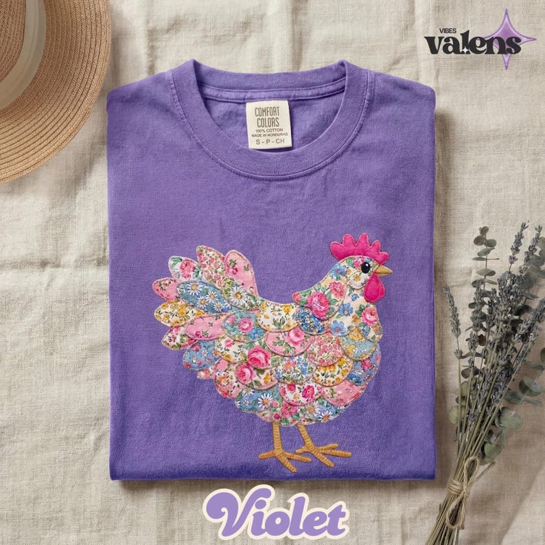 May include: A violet-colored t-shirt with a floral chicken design. The chicken is made of fabric with a variety of floral patterns in pink, blue, and white. The shirt has a crew neck and short sleeves. The word "Violet" is written in a script font at the bottom.