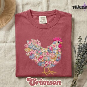May include: Crimson-colored t-shirt with a floral chicken design. The chicken is made of fabric with pink, blue, and yellow floral patterns. The shirt has a crew neck and short sleeves. The brand name "Comfort Colors" is visible on the tag.