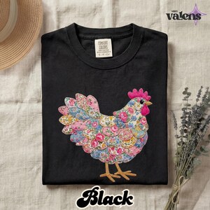 May include: Black t-shirt featuring a colorful chicken design. The chicken is made of fabric with floral patterns in pink, blue, and yellow. The word "Black" is written in a cursive font at the bottom of the shirt.