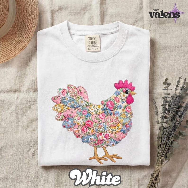 May include: White t-shirt featuring a colorful floral chicken design. The chicken has a pink comb and wattle, with a body made of various floral patterns in pink, blue, and yellow. The shirt has a Comfort Colors tag and the word "White" at the bottom.