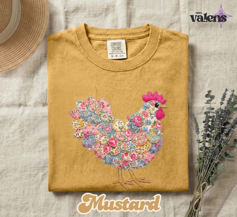 May include: Mustard-colored t-shirt with a floral chicken design. The chicken is made of various floral patterns in pink, blue, and white. The shirt has a crew neck and short sleeves. The text "Mustard" is at the bottom.