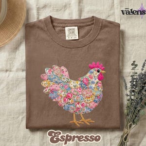 May include: Espresso-colored t-shirt featuring a colorful floral chicken design. The chicken has a pink comb and beak, with a body made of various floral patterns. The shirt is labeled "Comfort Colors" and "S-P-CH".