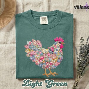 May include: A light green t-shirt featuring an embroidered chicken design. The chicken has a pink comb and wattle, with a body made of floral fabric in pink, blue, and yellow. The text "Light Green" is at the bottom.