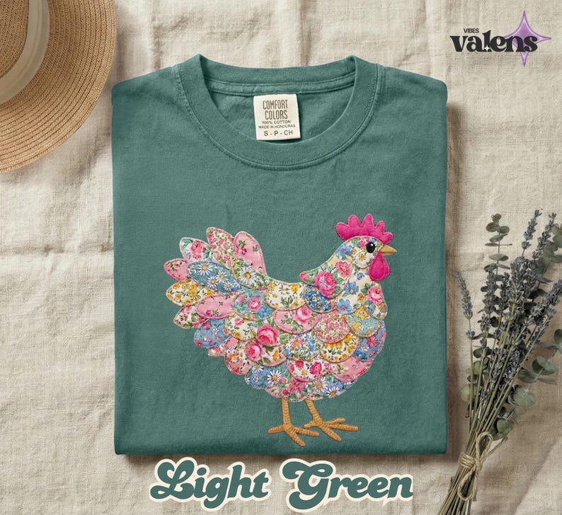 May include: A light green t-shirt featuring an embroidered chicken design. The chicken has a pink comb and wattle, with a body made of floral fabric in pink, blue, and yellow. The text "Light Green" is at the bottom.