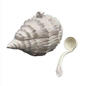 May include: A ceramic lidded tureen shaped like a large conch shell with a pearlescent finish and a small sculpted snail on the lid, accompanied by a matching long-handled ladle with a shell-shaped detail at the end of the handle.