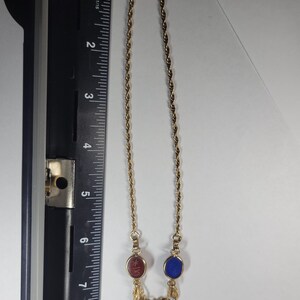 Puede incluir: Un collar de cadena trenzada dorada con tres piedras cabuj&oacute;n ovaladas en rojo, azul y verde, con un detalle met&aacute;lico floral sobre la piedra verde. Una regla negra muestra una longitud de aproximadamente 20,3 cm.