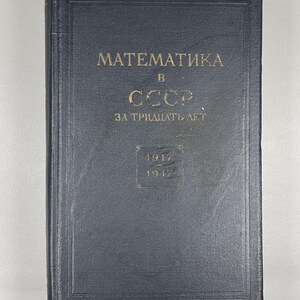 Op de afbeelding: Een donkerblauw boek met gouden letters. De titel luidt "MATEMATИKA B CCCP ЗА ТРИДЦАТЬ ЛЕТ" in Cyrillisch schrift. De jaren 1917 en 1947 zijn ook zichtbaar op de kaft. Het boek heeft een versleten uiterlijk.