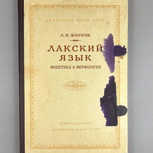 May include: A vintage book with a cream-colored cover featuring Cyrillic text and decorative borders. The title, "LAKSKIY YAZYK," is prominently displayed. The cover has purple stains. The book is from the Academy of Sciences of the USSR.