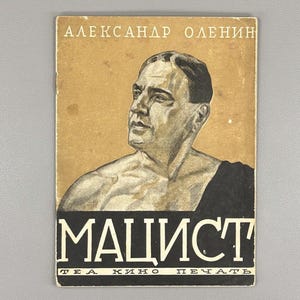 以下が含まれることがあります： 男性の肖像画と白い文字で「MAИCT」というタイトルが特徴のヴィンテージ本の表紙。上部には「АЛЕКСАНДР ОЛЕНИН」という名前があります。背景はベージュ色です。ヴィンテージ出版物です。