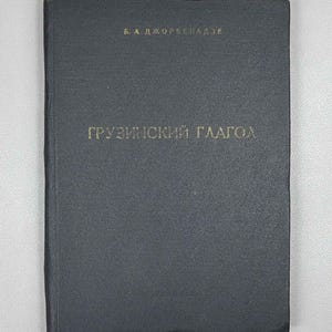 May include: A dark gray hardcover book with gold lettering on the front cover. The text at the top reads B. A. DZHORSBENADZE and the main title in the center reads GRUZINSKIY GLAGOL. The book has a textured, matte finish cover.