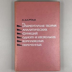 以下が含まれることがあります： 白文字と黒い水平線が入った、くすんだバラ色の本。タイトルはロシア語で、著者の名前であるA.カルタンが上にあります。この本は、解析関数に関する教科書のようです。