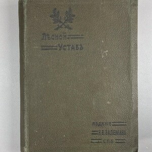 May include: An olive green book with embossed text and a decorative emblem. The cover features the title and author's name in dark lettering. The book's edges show signs of wear, suggesting it is an antique or vintage item.