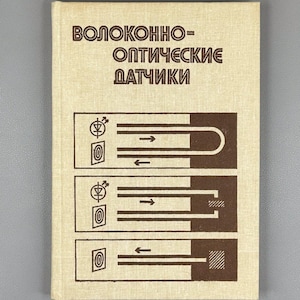 May include: A book with a beige cover featuring the title "ВОЛОКОННО-ОПТИЧЕСКИЕ ДАТЧИКИ" in brown letters. Below the title are three brown diagrams with arrows and symbols. The book has a textured appearance.