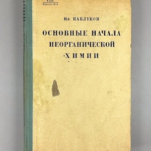 May include: A white ceramic mug with a black handle and the text "But First, Coffee" in a black, handwritten-style font. The mug is on a white surface.