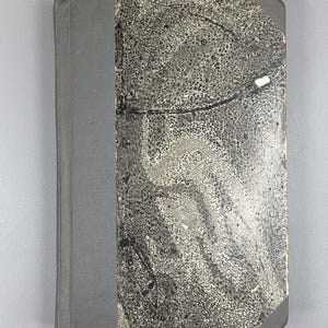 May include: A hardcover book with a gray spine and a cover featuring a black and white abstract pattern. The book's edges are slightly worn, suggesting it is vintage or well-used. The overall aesthetic is muted and classic.