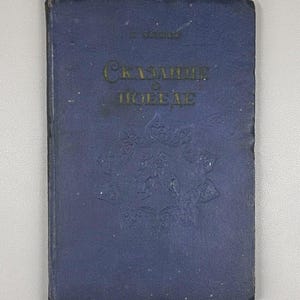 May include: A vintage blue book with gold lettering and embossed floral designs. The title "Сказание о Победе" is visible on the cover. The book has a worn appearance, suggesting it is an antique or a well-loved item.