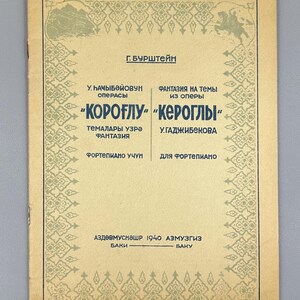 Può includere: Una copertina di spartito musicale vintage con testo in più lingue. La copertina è beige con un bordo decorativo e presenta il titolo "Koroglu" e il nome "G. Burshtein". Il testo è in nero e verde.
