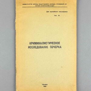 Op de afbeelding: Een vintage boekje met een lichtbruine papieren omslag en zwarte cyrillische tekst. Op de omslag staat "МИНИСТЕРСТВО ОХРАНЫ ОБЩЕСТВЕННОГО ПОРЯДКА ГРУЗИНСКОЙ ССР", "НАУЧНО-ТЕХНИЧЕСКИЙ ОТДЕЛ", "Для служебного пользования", "КРИМИНАЛИСТИЧЕСКОЕ ИССЛЕДОВАНИЕ ПОЧЕРКА", "Тбилиси" en "1968".