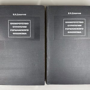 Puede incluir: Dos libros de tapa dura negros con el título "BANKROTSTVO STRATEGII GERMANSKOGO FASHIZMA" en texto blanco. El nombre del autor, "V.I. Dashichev", está impreso encima del título. Los libros están uno al lado del otro.