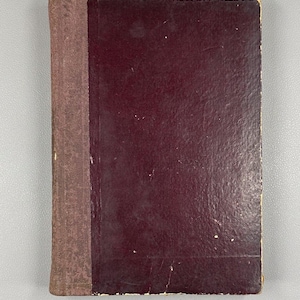 Może przedstawiać: Stara książka z bordową okładką i brązowym grzbietem. Okładka nosi ślady użytkowania, z drobnymi niedoskonałościami. Grzbiet jest w jaśniejszym odcieniu brązu, a książka wydaje się być mocno używana.
