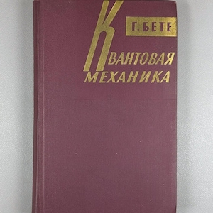 May include: A maroon book with gold lettering and text in Russian. The title reads "Quantum Mechanics" and the author's name is also displayed. The book has a textured cover and is likely a textbook.