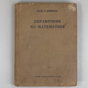 Op de afbeelding: Een vintage, bruinachtig boek met de titel "Справочник по математике" in vette, zwarte Cyrillische letters. De omslag bevat ook de naam "Проф. Г. дуввель" en de tekst "онти-нктп-ссср-1936". Het boek heeft een versleten uiterlijk.