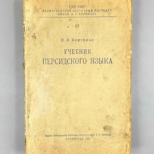 Op de afbeelding: Een vintage leerboek met een versleten, bruinachtige kaft. De titel, "УЧЕБНИК ПЕРСИДСКОГО ЯЗЫКА" (Leerboek Perzische taal), is prominent aanwezig. De naam van de auteur, "Е. Э. Бертельс", en de naam van het Leningradse Oosterse Instituut zijn ook zichtbaar.