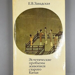 Pode incluir: Um livro vintage com uma capa bege. A capa apresenta uma ilustração circular de figuras numa varanda. O título está em russo, com o nome do autor no topo. O título do livro é "Problemas estéticos da pintura chinesa antiga."