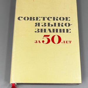 May include: A vintage book with a light yellow cover. The title, in black Cyrillic letters, reads "Soviet Linguistics" with the number "50" in red. A red ribbon bookmark is visible.