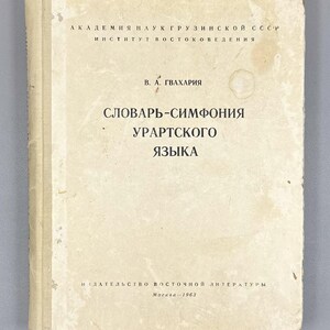 May include: A vintage book with a worn, off-white cover. The title, in Cyrillic script, reads "SLOVAR'-SIMFONIYA URARTSKOGO YAZYKA". The book's cover also features text in Cyrillic and the year 1963.