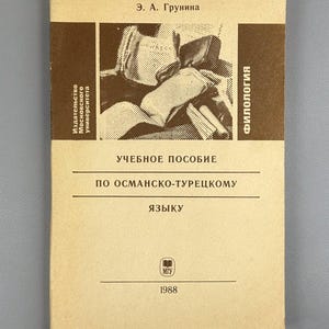 Op de afbeelding: Een vintage boekcover in beige en bruin, met Russische tekst. De cover bevat de tekst "УЧЕБНОЕ ПОСОБИЕ" en "ПО ОСМАНСКО-ТУРЕЦКОМУ ЯЗЫКУ". Het jaar 1988 staat onderaan gedrukt. Het boek is een leerboek filologie.