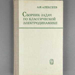 Può includere: Un libro con copertina e dorso beige chiaro. Il titolo è in russo, con testo verde. Il nome dell'autore è in alto. Un piccolo emblema verde è in basso a destra. Il libro è su una superficie grigia.