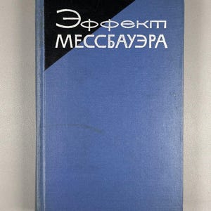 May include: A hardcover book with a blue cover and the title "Эффект Мессбауэра" in white lettering. The top left corner of the book has a black triangle. The book appears to be in good condition.