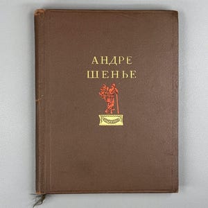 May include: A brown hardcover book with the title "ANDRE SHENYE" in gold lettering. A gold illustration of a person with a staff and foliage is centered below the title. The book has a worn appearance.