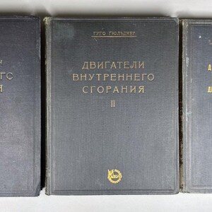 Puede incluir: Tres libros antiguos con cubiertas de color gris oscuro y letras doradas. Los títulos están en ruso, los dos primeros volúmenes se titulan "Motores de combustión interna" y el tercero "Artículos adicionales". Cada libro presenta un emblema dorado.