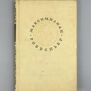 May include: A vintage book with a cream-colored cover featuring the name "Максимилиан Робеспьер" in a circular design around a portrait. The book's spine has a dark brown stripe, and the text "ГОСПОЛИТИЗДАТ. 1953" is printed at the bottom.